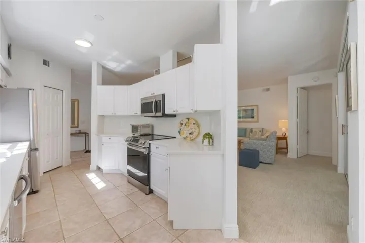 Kitchen featuring stainless steel appliances, white cabinets, light colored carpet, and light tile patterned flooring