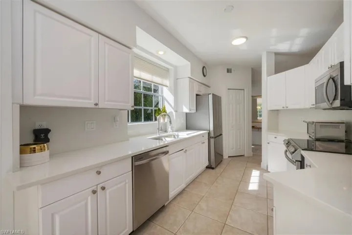 Kitchen featuring white cabinets, stainless steel appliances, light tile patterned floors, and light stone countertops