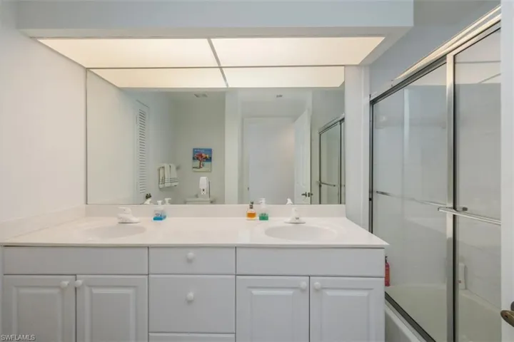 Bathroom featuring double vanity and bath / shower combo with glass door
