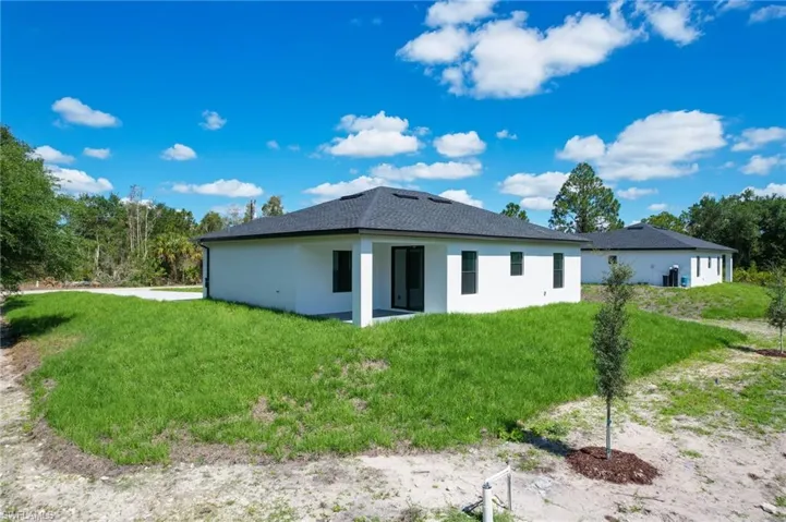 Back of property with stucco siding, a lawn, and roof with shingles
