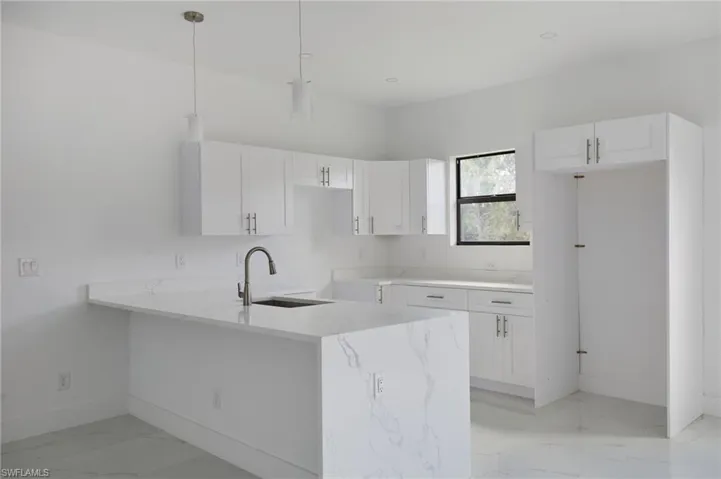 Kitchen featuring baseboards, light marble finish flooring, a sink, white cabinetry, and a peninsula