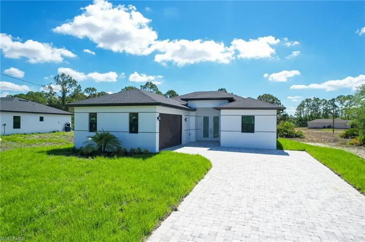 View of front of home with french doors, decorative driveway, an attached garage, stucco siding, and a front yard