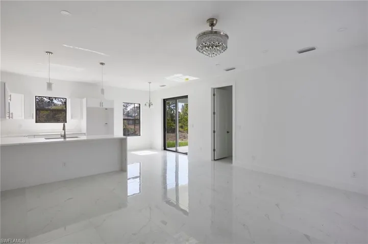 Unfurnished living room featuring a sink, a chandelier, light marble finish floors, baseboards, and recessed lighting