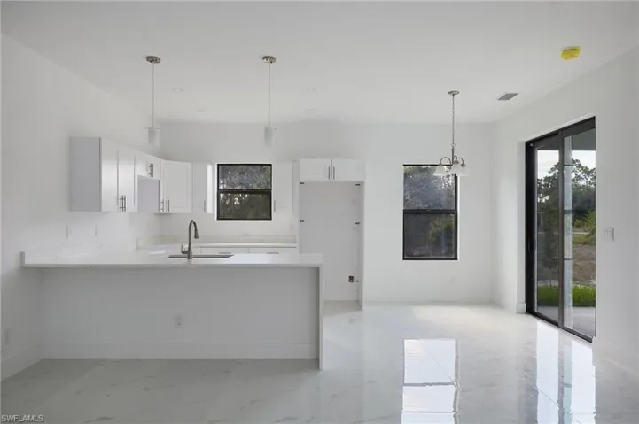 Kitchen featuring a sink, a peninsula, light marble finish floors, white cabinetry, and light countertops