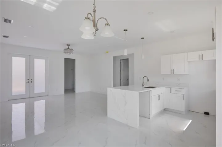 Kitchen featuring a sink, a peninsula, white cabinetry, french doors, and pendant lighting
