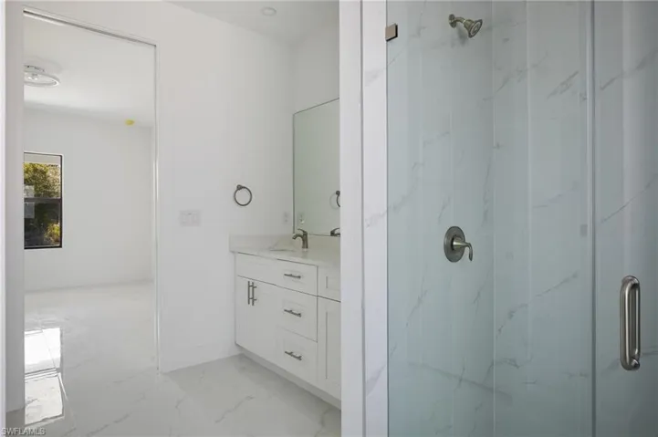 Full bath with marble look tile flooring, a marble finish shower, vanity, and baseboards