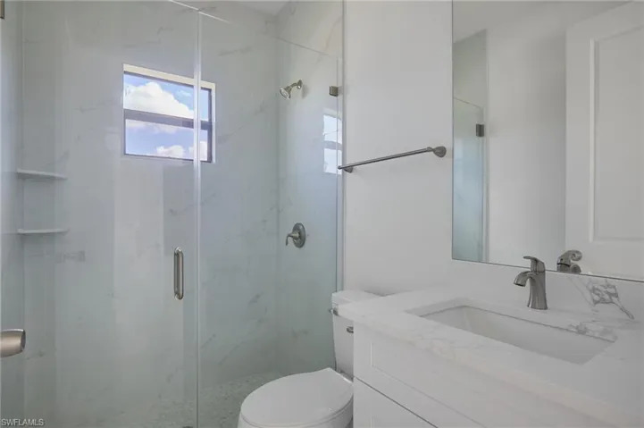 Bathroom with toilet, a marble finish shower, and vanity
