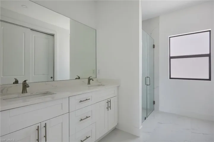 Primary Bathroom with baseboards, marble finish flooring, a shower stall, and double vanity