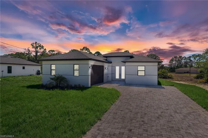 View of front facade featuring an attached garage, a lawn, decorative driveway, and stucco siding