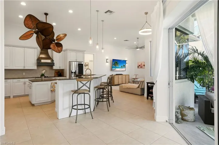 Kitchen featuring a kitchen island with sink, ceiling fan, white cabinetry, pendant lighting, and a kitchen bar