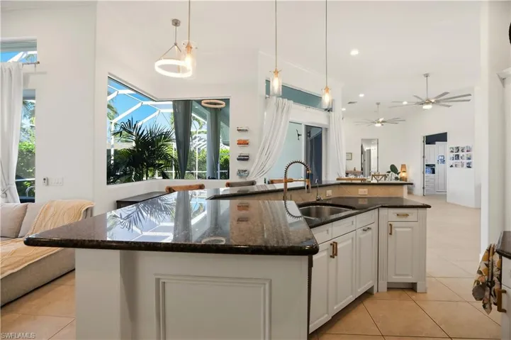 Kitchen featuring dark stone counters, open floor plan, white cabinets, an island with sink, and light tile patterned floors