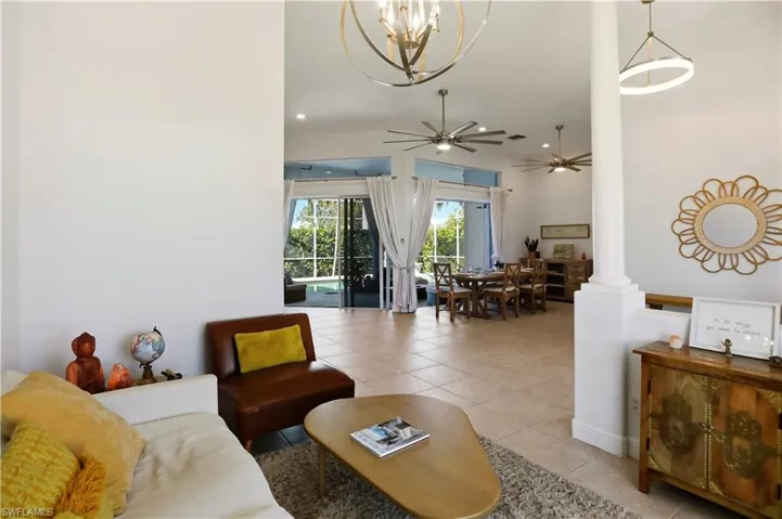 Living area with light tile patterned flooring, a ceiling fan, ornate columns, a chandelier, and recessed lighting