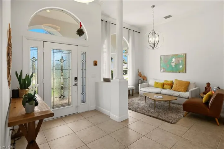 Foyer with ornate columns, light tile patterned floors, healthy amount of natural light, and ornamental molding