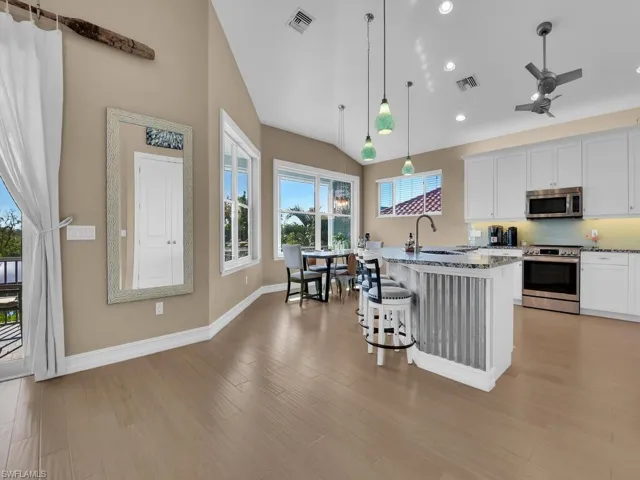 Kitchen with appliances with stainless steel finishes, light wood-type flooring, pendant lighting, white cabinetry, and a breakfast bar area