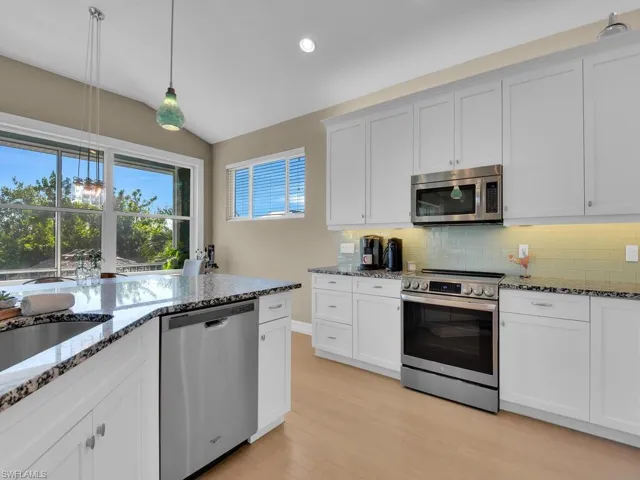 Kitchen featuring light wood-type flooring, stainless steel appliances, vaulted ceiling, pendant lighting, and white cabinetry