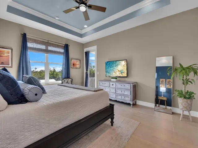 Bedroom with ceiling fan, ornamental molding, a tray ceiling, and light hardwood / wood-style flooring