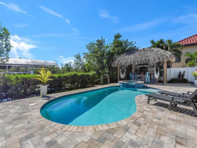 View of swimming pool with a tiki hut, a patio area, and an in ground hot tub