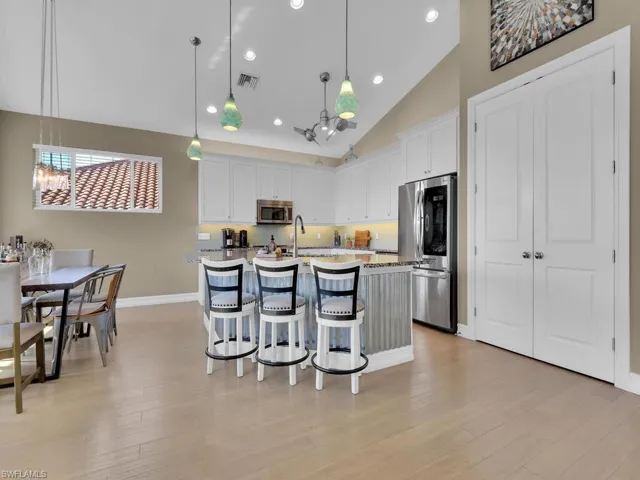 Kitchen featuring white cabinets, decorative light fixtures, stainless steel appliances, and a kitchen island with sink