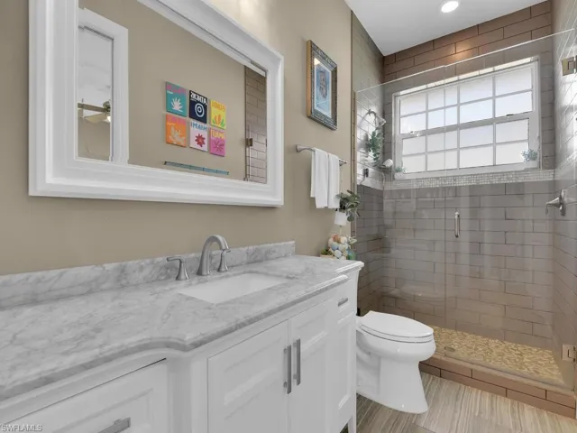 Bathroom with an enclosed shower, vanity, toilet, and tile patterned flooring