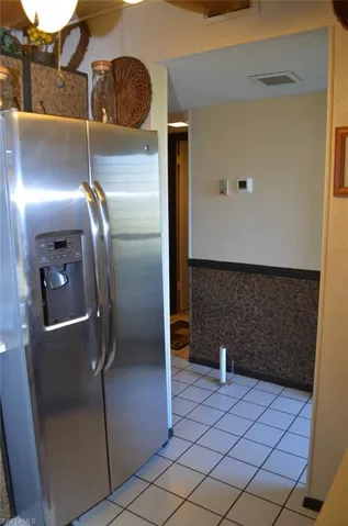Kitchen featuring stainless steel fridge with ice dispenser, light tile patterned flooring, and a wainscoted wall