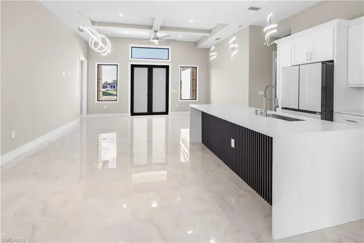 Kitchen featuring light stone counters, freestanding refrigerator, open floor plan, white cabinets, and coffered ceiling