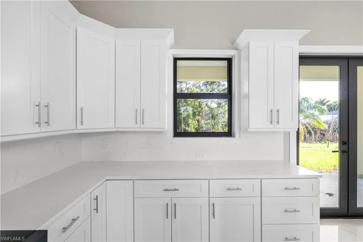 Kitchen with white cabinets, light stone countertops, decorative backsplash, and french doors
