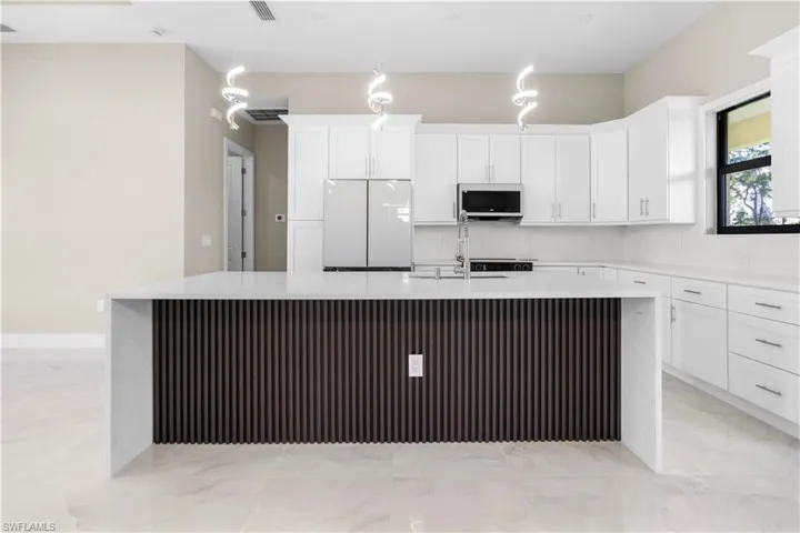 Kitchen with a large island, white appliances, light stone countertops, and white cabinets