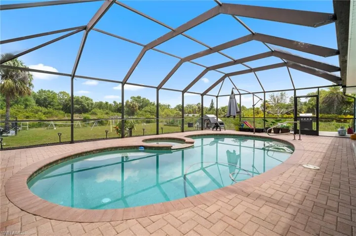 View of swimming pool with a pool with connected hot tub, a patio area, view of wooded area, a grill, and glass enclosure