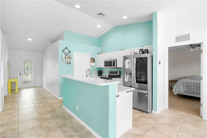 Kitchen with stainless steel appliances, light countertops, white cabinets, light tile patterned floors, and baseboards