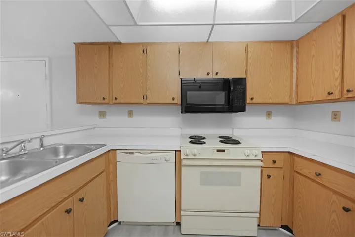 Kitchen with sink, light wood-type flooring, white appliances, and a paneled ceiling