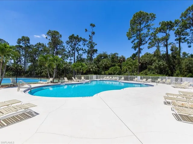Community pool with view of wooded area, a patio, and a tennis court