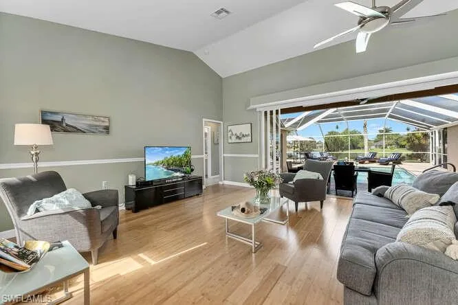 Living area with a sunroom, a ceiling fan, high vaulted ceiling, wood finished floors, and baseboards