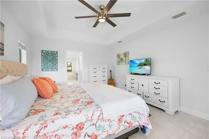 Bedroom featuring a tray ceiling, ceiling fan, ensuite bathroom, and light tile patterned floors