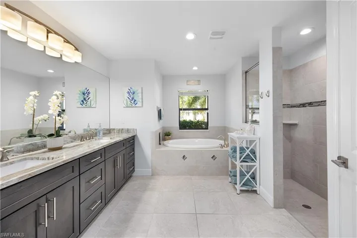 Bathroom featuring double vanity, a bath, walk in shower, and recessed lighting