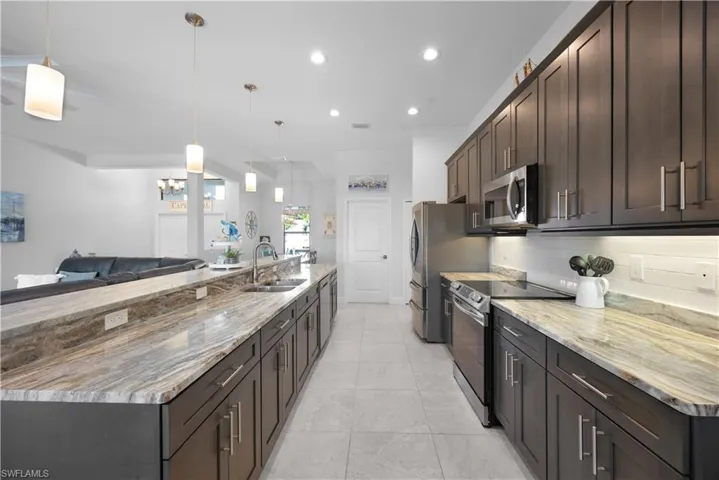 Kitchen with stainless steel appliances, decorative light fixtures, open floor plan, light stone countertops, and dark brown cabinets