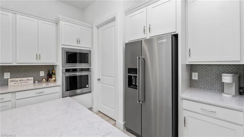 Kitchen featuring backsplash, stainless steel appliances, light stone counters, and white cabinetry