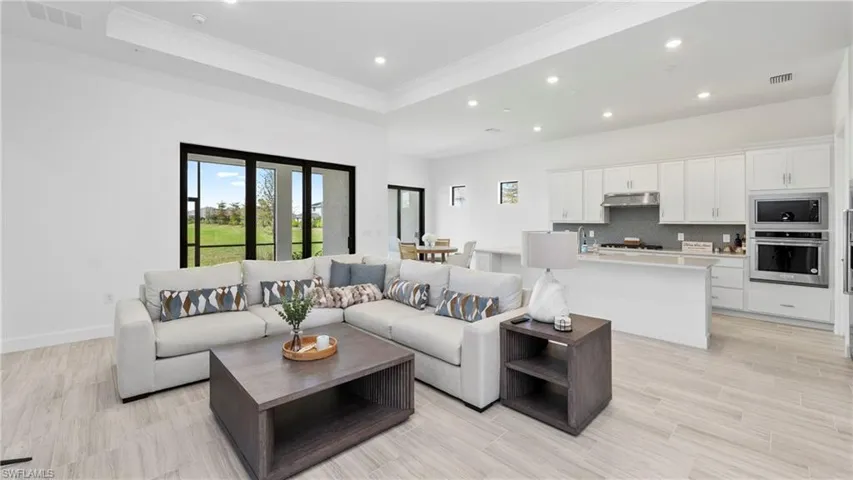 Living room featuring a tray ceiling, recessed lighting, light wood finished floors, and crown molding