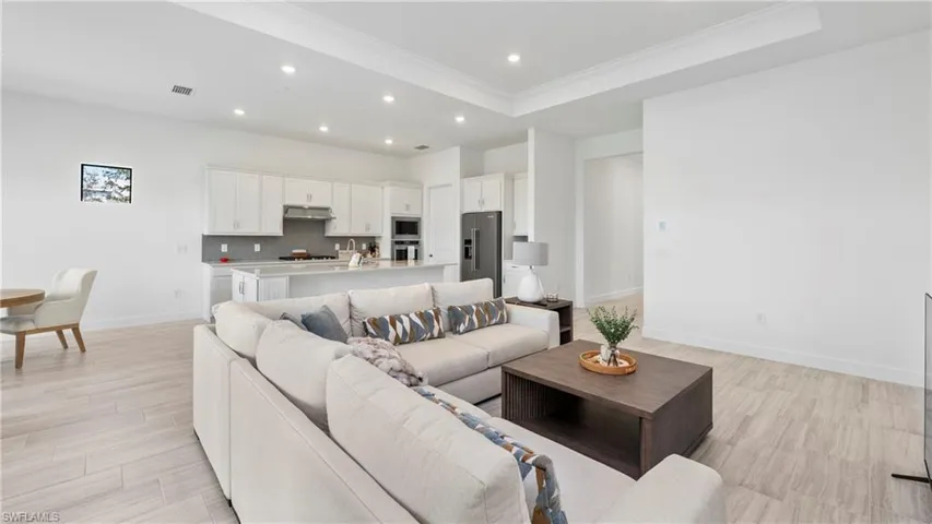 Living room with light wood-type flooring, a tray ceiling, recessed lighting, and crown molding
