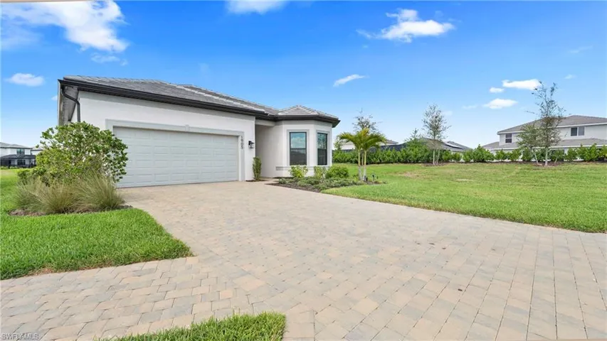 View of front of house with a front yard, an attached garage, stucco siding, and decorative driveway