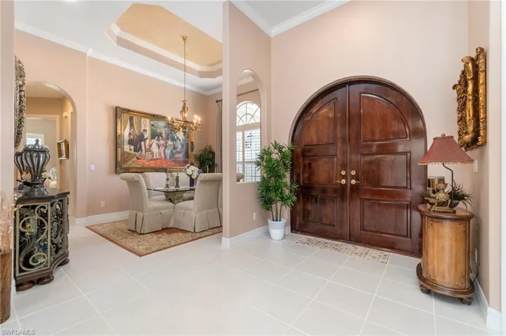 Tiled entryway featuring baseboards, a notable chandelier, crown molding, and arched walkways