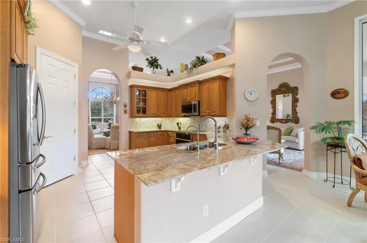 Kitchen featuring a peninsula, stainless steel appliances, arched walkways, a sink, and brown cabinetry