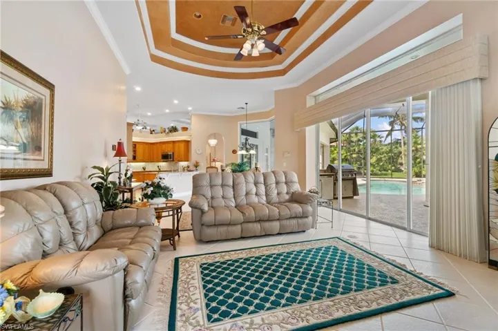 Living area featuring a tray ceiling, light tile patterned floors, ornamental molding, and a ceiling fan