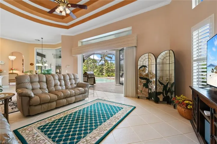 Living area with a tray ceiling, ceiling fan, tile patterned floors, and crown molding