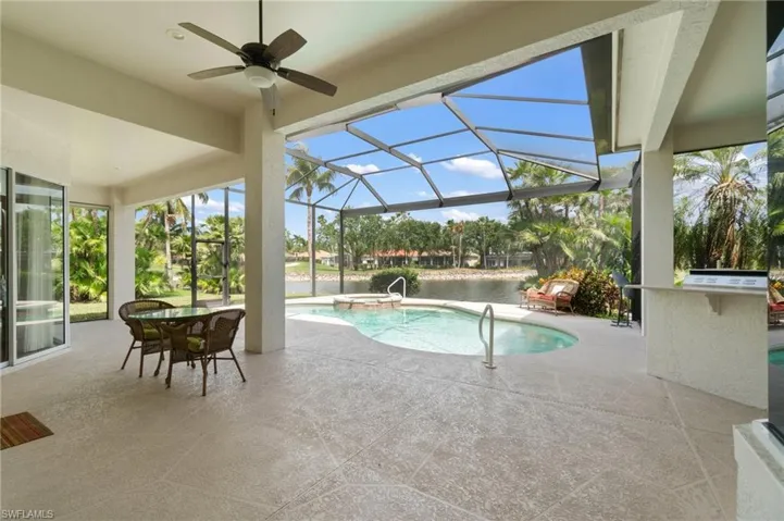 View of swimming pool featuring glass enclosure, a pool with connected hot tub, ceiling fan, and a patio area