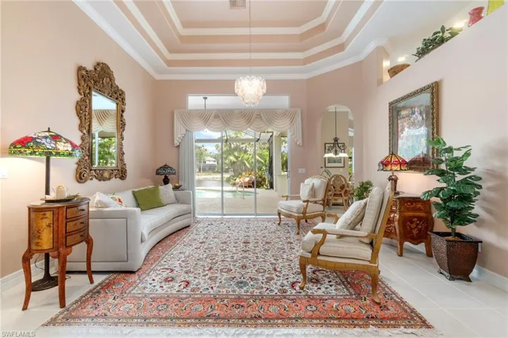 Living area with tile patterned flooring, a tray ceiling, crown molding, baseboards, and a notable chandelier
