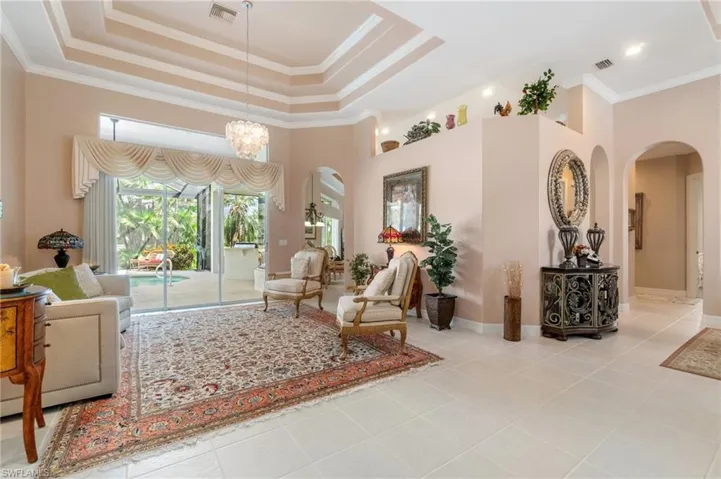 Living room with a tray ceiling, visible vents, and arched walkways