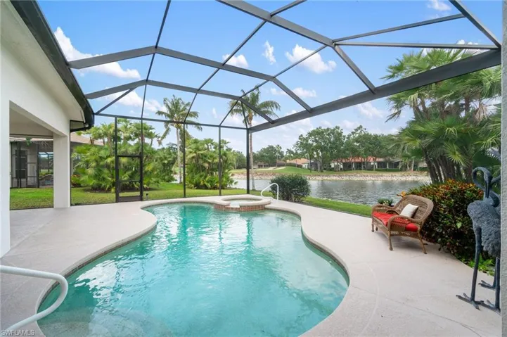 View of swimming pool with a patio, a water view, a pool with connected hot tub, and glass enclosure
