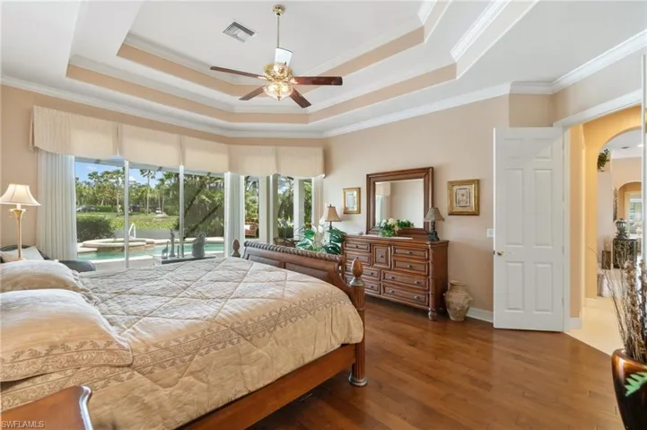 Bedroom featuring a tray ceiling, access to outside, wood-type flooring, visible vents, and arched walkways