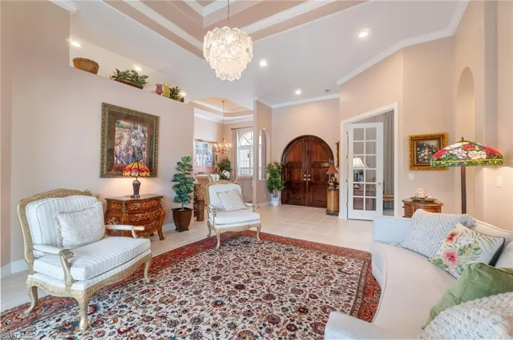 Living room featuring tile patterned flooring, a raised ceiling, ornamental molding, and an inviting chandelier