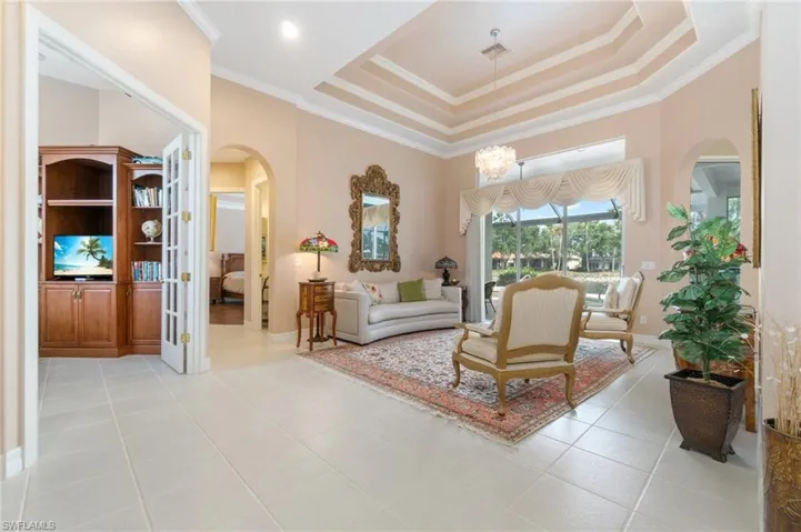 Living room with arched walkways, ornamental molding, a tray ceiling, and light tile patterned flooring